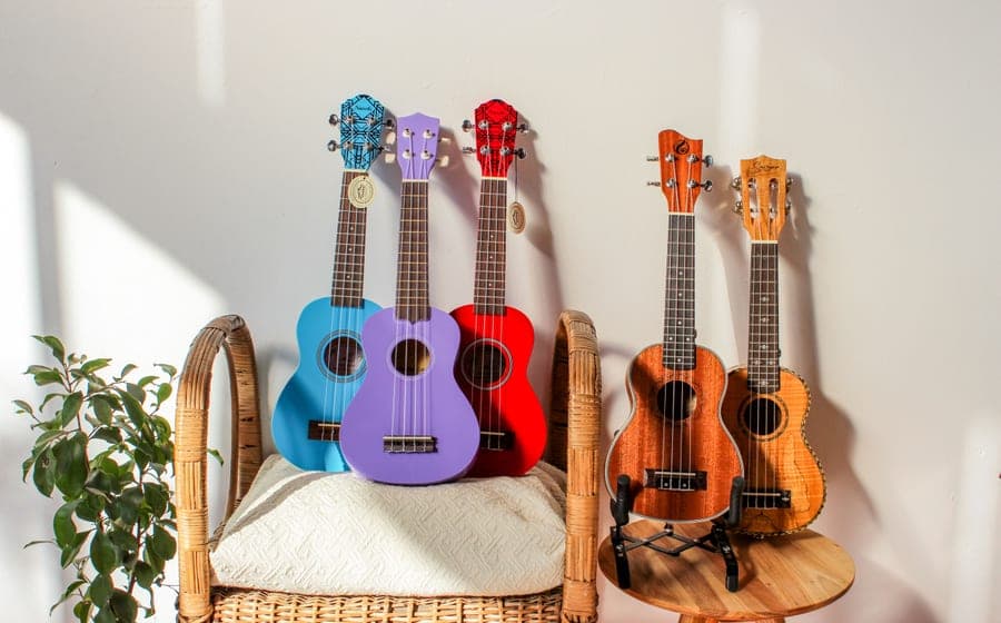 A wooden soprano ukulele resting on a table beside a window